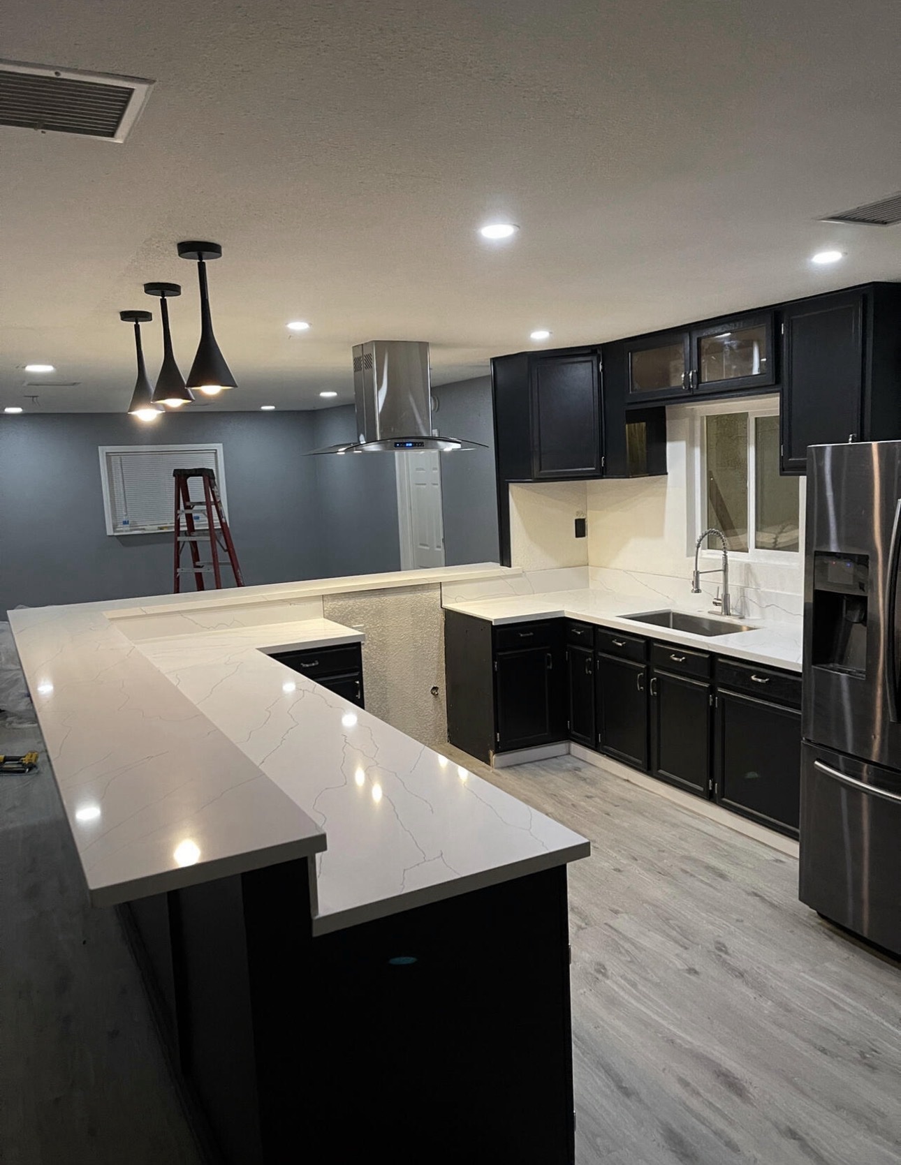Nearly finished open-concept kitchen with black cabinetry, white marble-look counters, an island range hood and black pendant lights