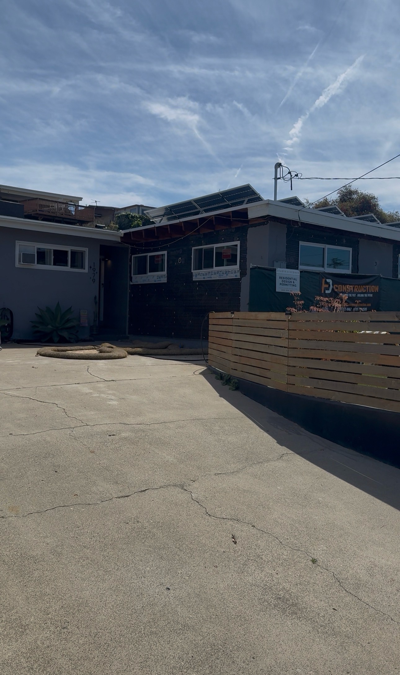 Galveston project exterior under construction with a site fence, exposed roof framing and permit signage