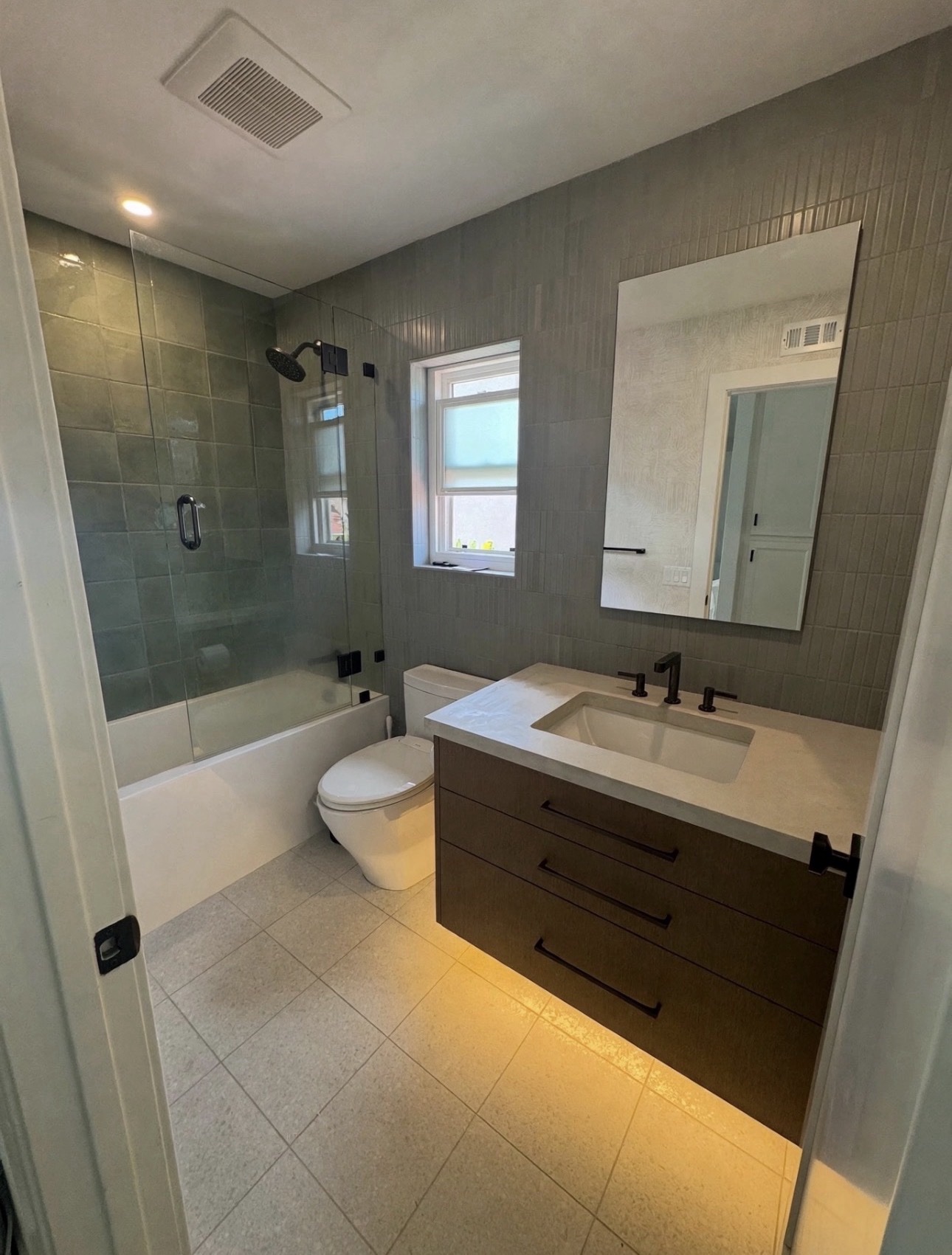 Carlsbad guest bathroom with green-gray tile, a glass tub and shower enclosure, and a floating vanity with underglow lighting