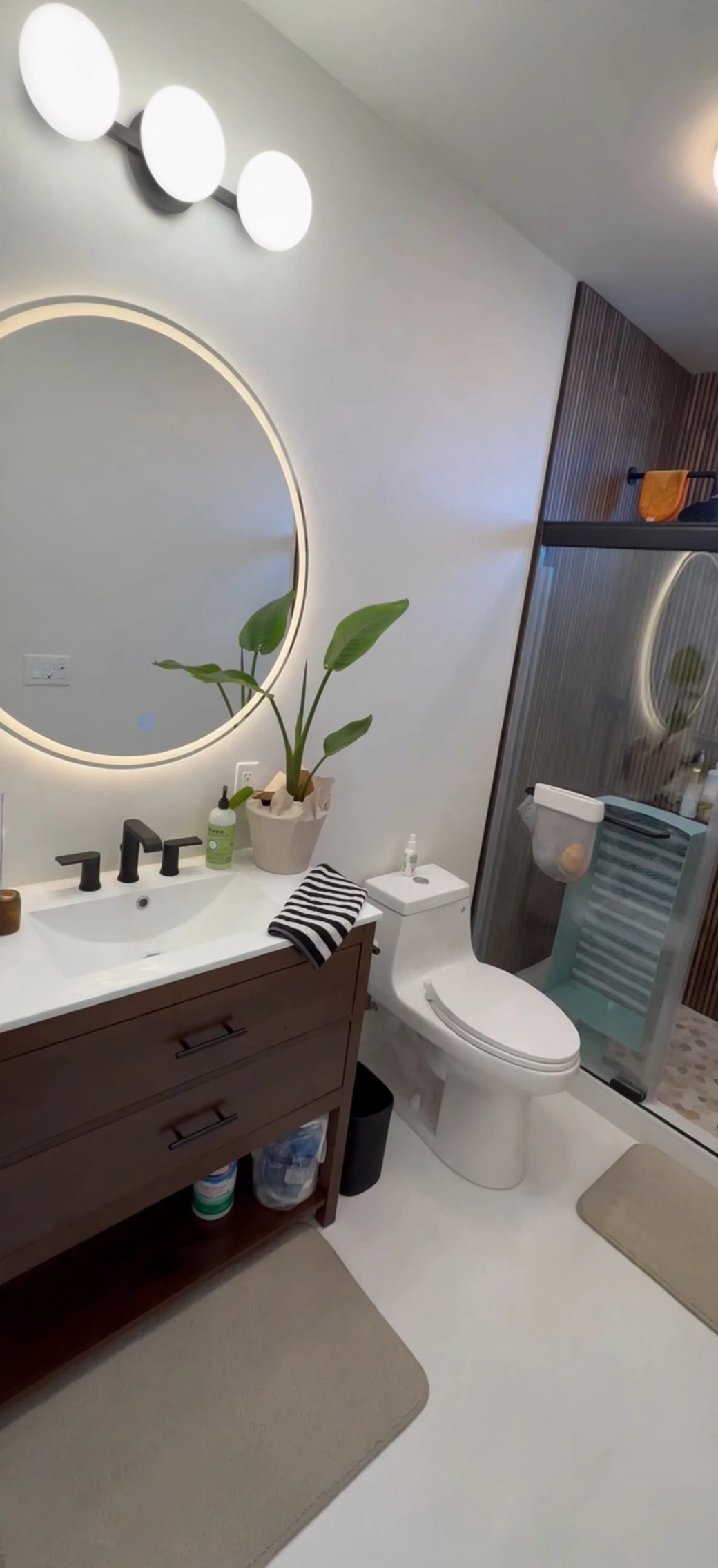 Finished Galveston ADU bathroom with a dark wood vanity, illuminated round mirror and walk-in shower